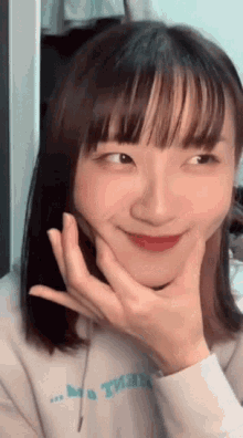 a young woman with bangs is smiling and holding her hand to her face .