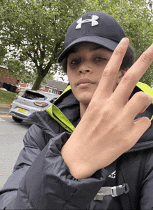 a man wearing a black under armour hat holds up his fingers