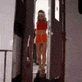 a woman in a red crop top and shorts is standing in a doorway .