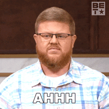 a man wearing glasses and a plaid shirt says ahh