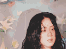 a woman with long black hair is standing in front of flowers