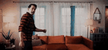 a man is standing in a living room next to a red couch .