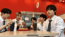 a group of young men are sitting at a table in front of a red wall with a number 0 on it
