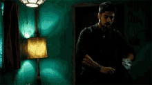 a man with a tattoo on his arm is standing in a dark room next to a lamp