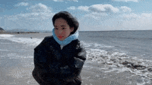 a woman wearing a scarf and a jacket is standing on the beach