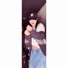a woman wearing a ny hat and a crop top is standing in a dark room