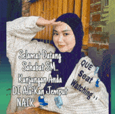 a woman wearing a hijab and a striped shirt that says que seat watching