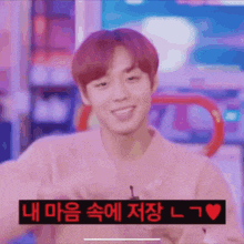 a young man with red hair is smiling and making a heart shape with his hands .