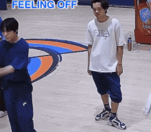 two young men are standing on a basketball court and one of them is wearing a fila shirt .