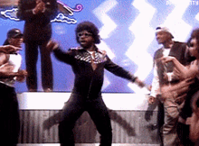 a man in a black jacket is dancing on a stage in front of a crowd of people