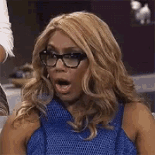 a woman wearing glasses and a blue dress has her mouth open