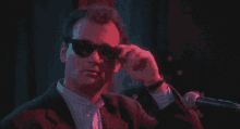 a man wearing sunglasses adjusts his glasses while standing in front of a microphone