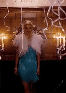 a woman in a blue dress and white feathers is standing in a room with balloons and streamers .