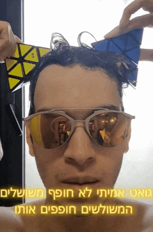a man wearing sunglasses is holding a yellow and blue cube on his head