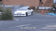 a white car is drifting down a road with people standing behind it .