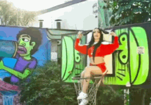 a woman is sitting in a basketball hoop in front of graffiti