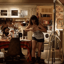 a woman standing in a kitchen wearing a tank top that says shepherd on it