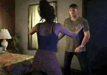 a man and a woman are dancing in a bedroom with a lamp on the nightstand