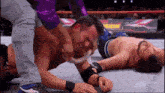 two men are wrestling in a wrestling ring and one of them is laying on the floor .