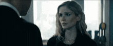 a man and a woman are looking at each other in a room . the woman is wearing a necklace and earrings .