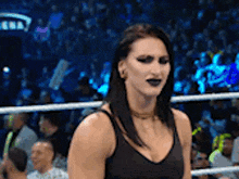 a woman in a black tank top is standing in a wrestling ring with a crowd watching .