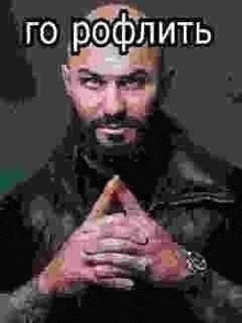 a man with a beard and a watch is sitting with his hands folded in front of him .