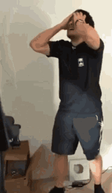 a man wearing shorts and a black shirt has his hands on his head while standing in a room