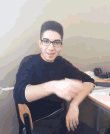 a young man wearing glasses is sitting at a desk