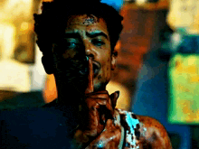 a man with a bloody face is holding his finger to his mouth