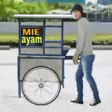 a man is pushing a cart with a sign that says mie ayam on it .