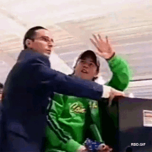 a man in a green jacket with the word lacoste on it is being held by another man