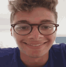 a young man wearing glasses and a blue shirt smiles for the camera .