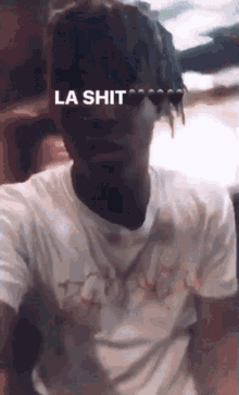 a man with dreadlocks is wearing a t-shirt that says ' la shit ' on it