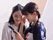 two girls are looking at a cell phone and one has a shirt that says hi