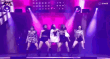 a group of young women are dancing on a stage in front of a pink background .