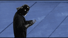a man wearing a darth vader helmet and gloves looks at his phone