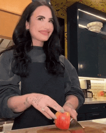 a woman in a black apron is cutting a red apple