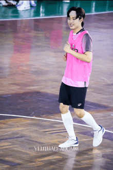 a man wearing a pink shirt and black shorts is running on a basketball court