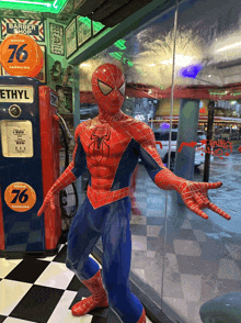 a statue of spider man standing in front of a gas pump that says 76 ethyl