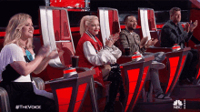 a group of people sitting in red chairs with the words #thevoice on the bottom right