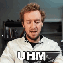 a man with a beard is reading a book and the word uhm is on the front of his shirt