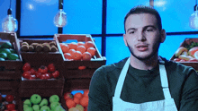 a man wearing an apron stands in front of crates of fruit
