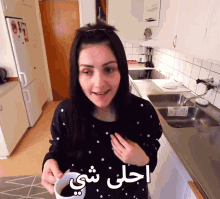 a woman in a kitchen holding a cup of coffee with arabic writing on the bottom