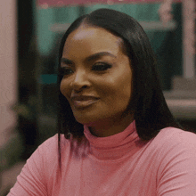 a woman wearing a pink turtleneck smiles at the camera