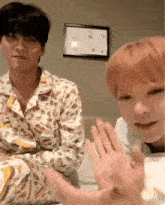two young men are sitting on a bed and one of them is waving his hand .