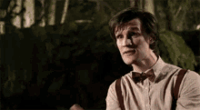 a man wearing a bow tie , suspenders and a shirt is standing in the woods .