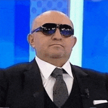 a bald man wearing sunglasses and a suit and tie is making a funny face .