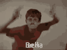 a young boy in a red shirt is making a funny face with his arms in the air while a woman looks on .