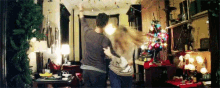 a man and a woman are dancing in a living room with a christmas tree in the background .