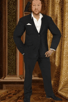 a man in a suit with his hands in his pockets stands in front of a gold curtain